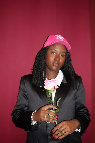 Portrait studio d'une membre de MTL Students sur fond cramoisi, tenant une rose.
