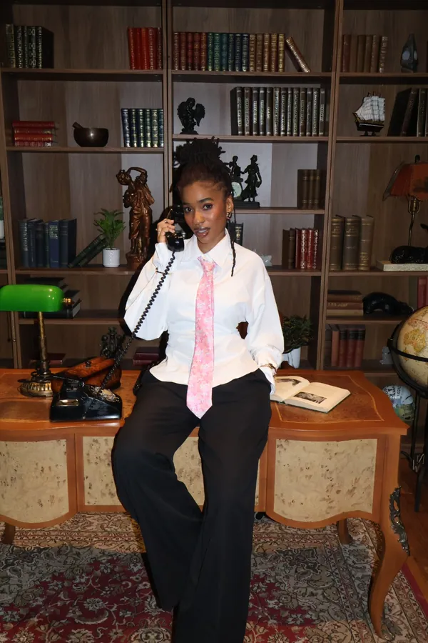 Portrait de l'équipe dans un décor de bibliothèque : une membre assise sur un bureau, cravate rose, un combiné téléphonique à l'oreille.