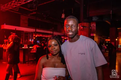 Deux étudiants posent ensemble dans une salle baignée de lumière rouge pendant une soirée.