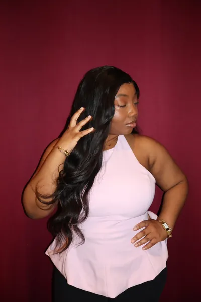 Portrait studio sur fond cramoisi : une membre de l'équipe en haut rose pâle, la main dans les cheveux.
