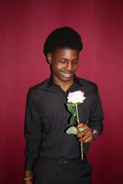 Portrait studio sur fond cramoisi : un membre de l'équipe habillé en noir sourit en regardant la rose qu'il tient.