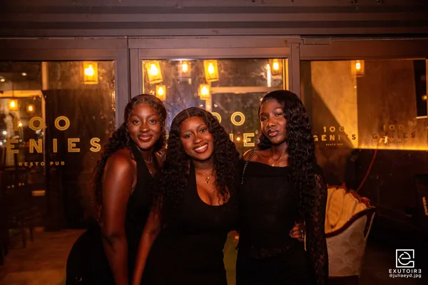 Trois étudiantes posent ensemble devant l'enseigne lumineuse du Resto-Pub 100 Génies.