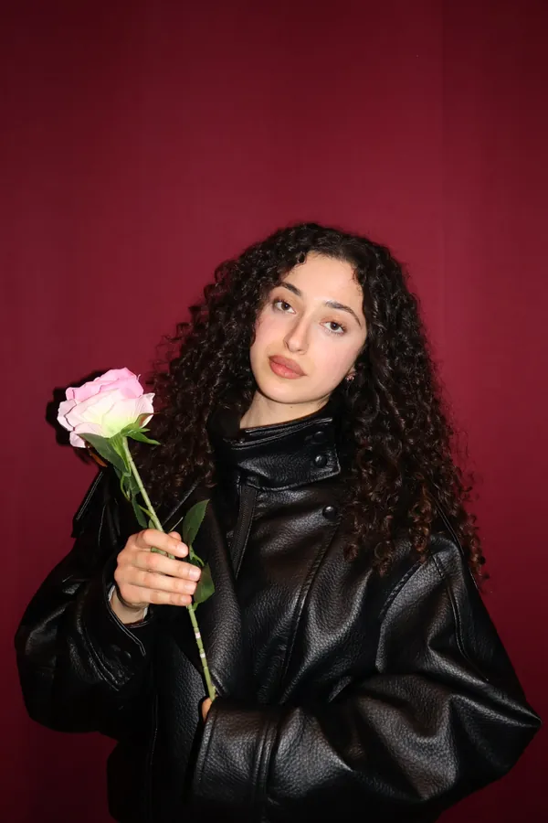 Portrait studio sur fond cramoisi : une membre de l'équipe en veste de cuir noire tient une rose.