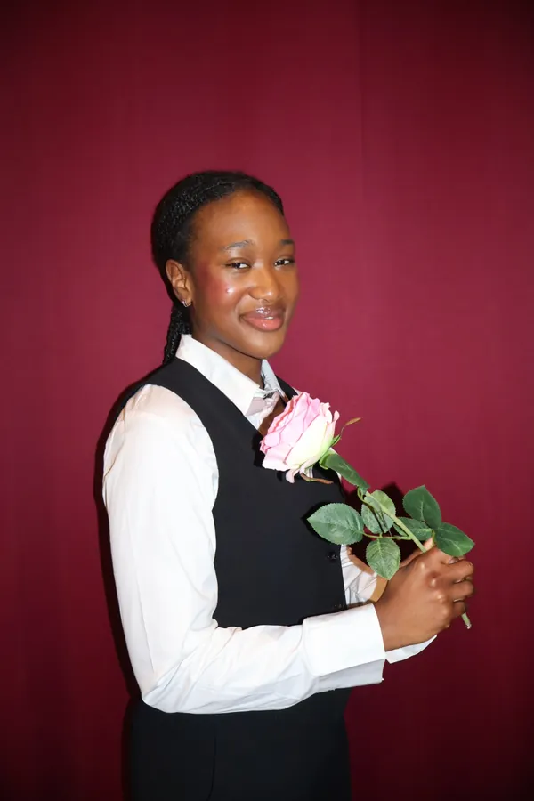 Portrait studio d'une membre de MTL Students de profil, gilet noir, tenant une rose sur fond cramoisi.
